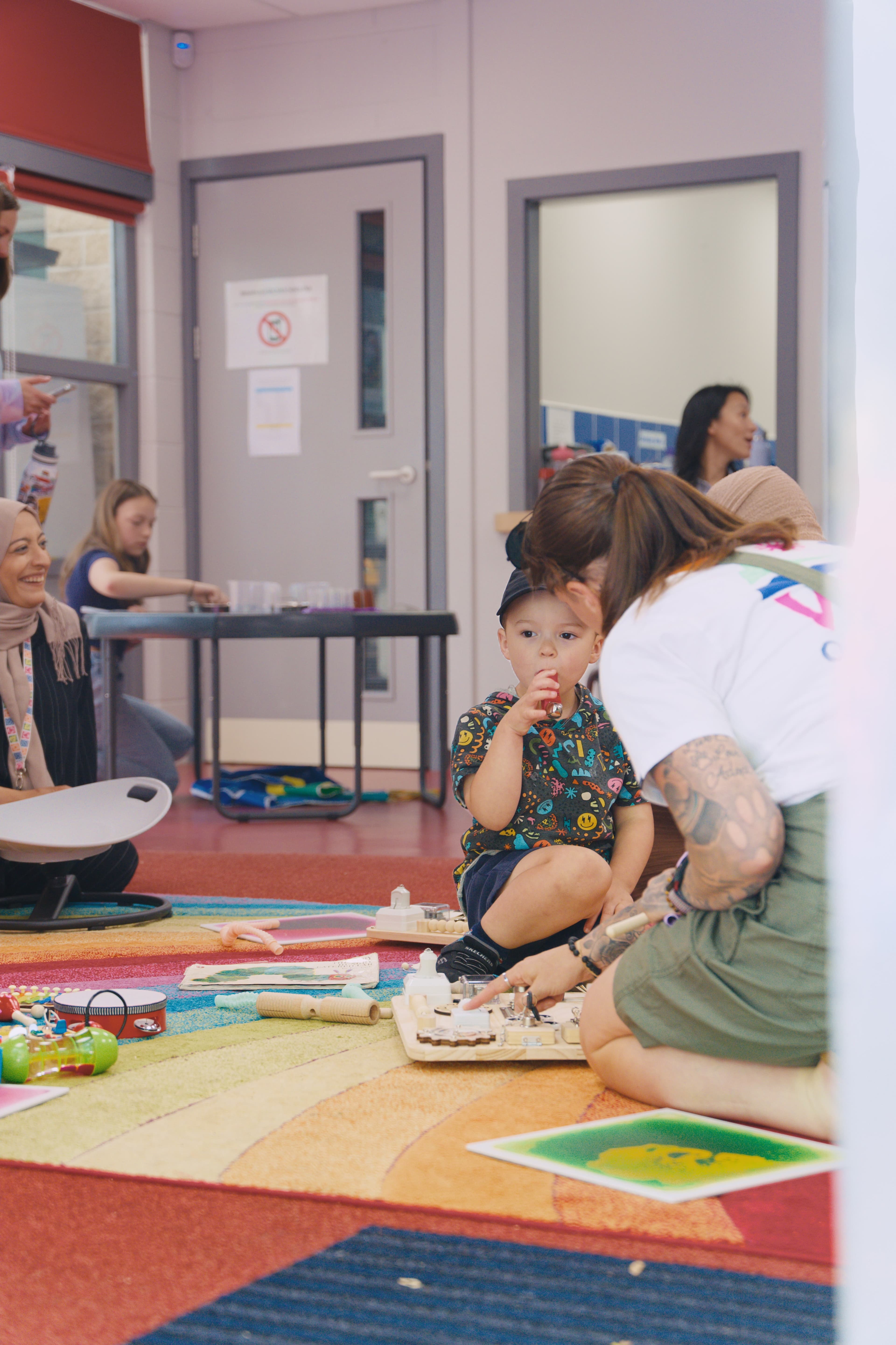 An adult and child exploring sensory boards together on a rainbow rug